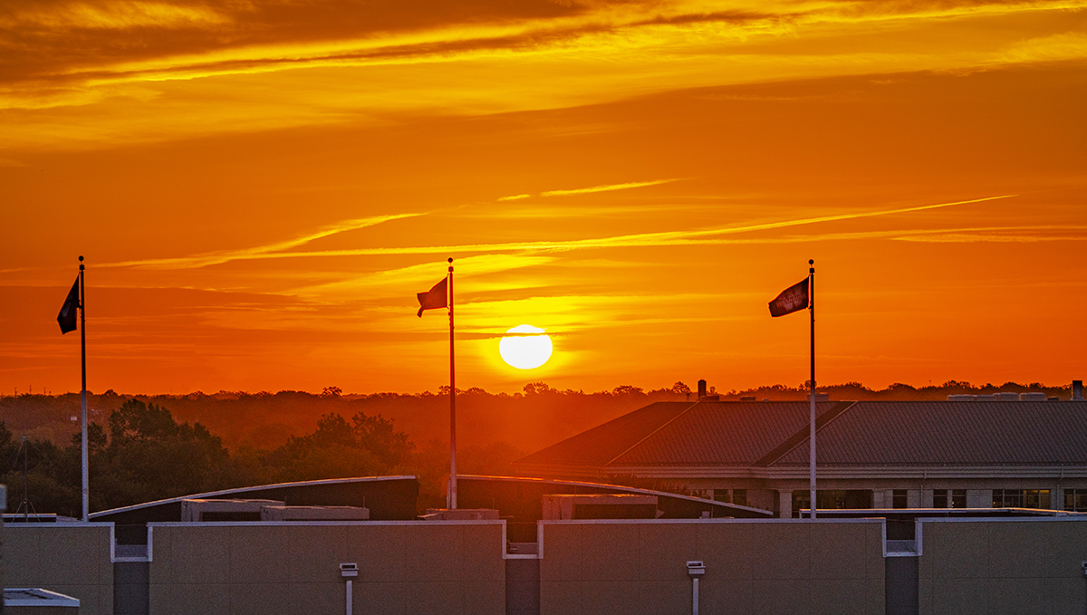 Sunrise over campus with three flags from Yager Stadium in the foreground