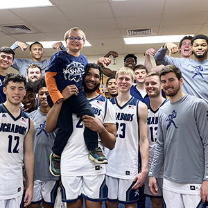 Men's basketball team and team impact player posing in the locker room