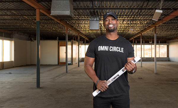 Michael Odupitan posing in the new building for Omni Circle, holding blue prints