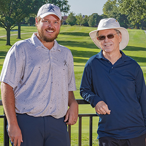 Two individuals pose in front of a golf course