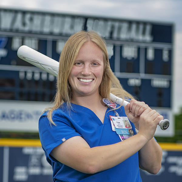 Paige Robbins poses with a softball bat in her nursing uniform