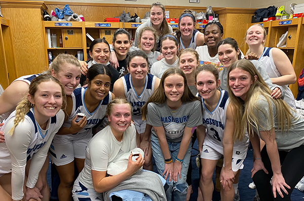 The women's basketball team and team impact player posing in the locker room